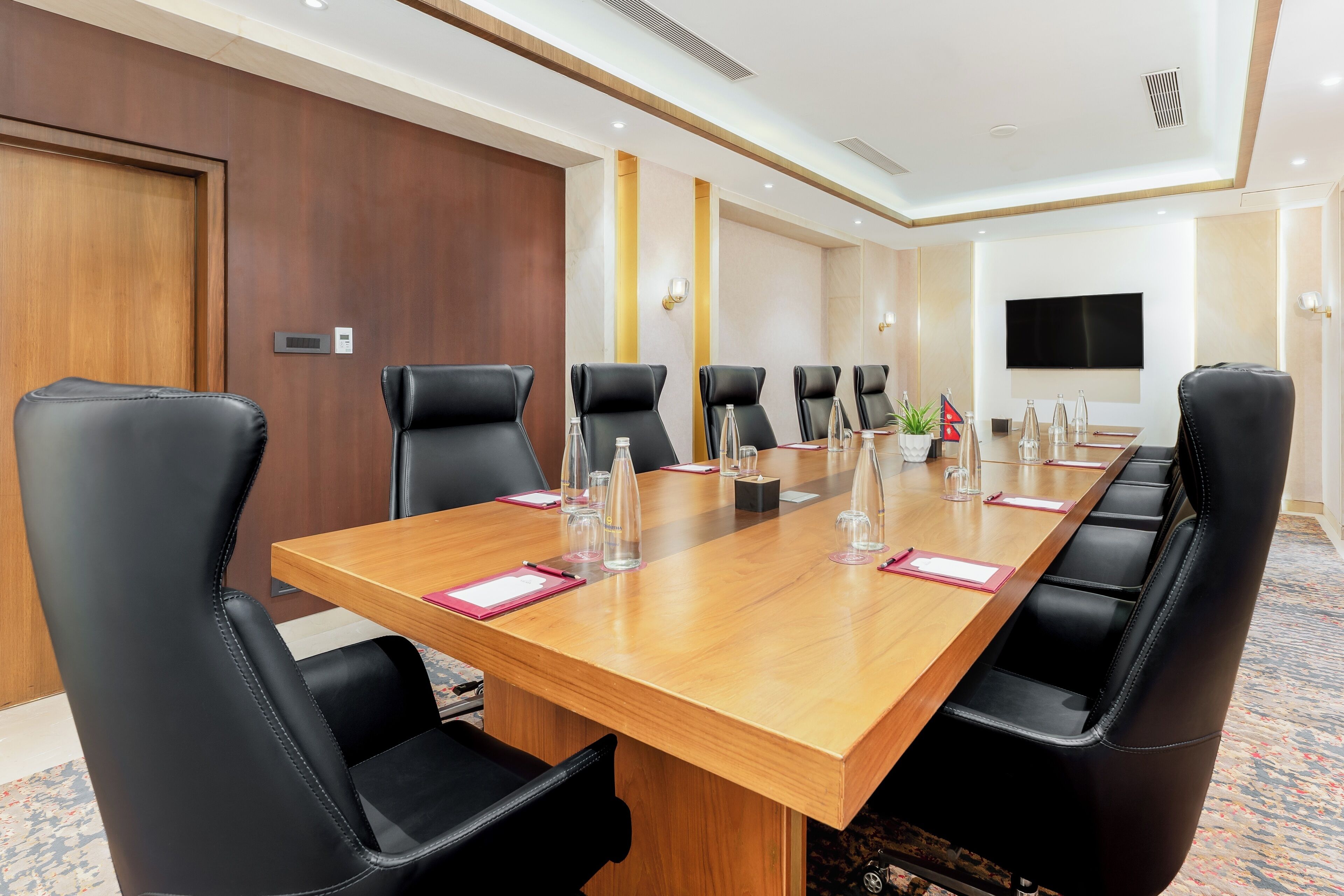 Un salón de conferencias con una larga mesa de madera, sillas de cuero negro y una televisión de pantalla plana en la pared.