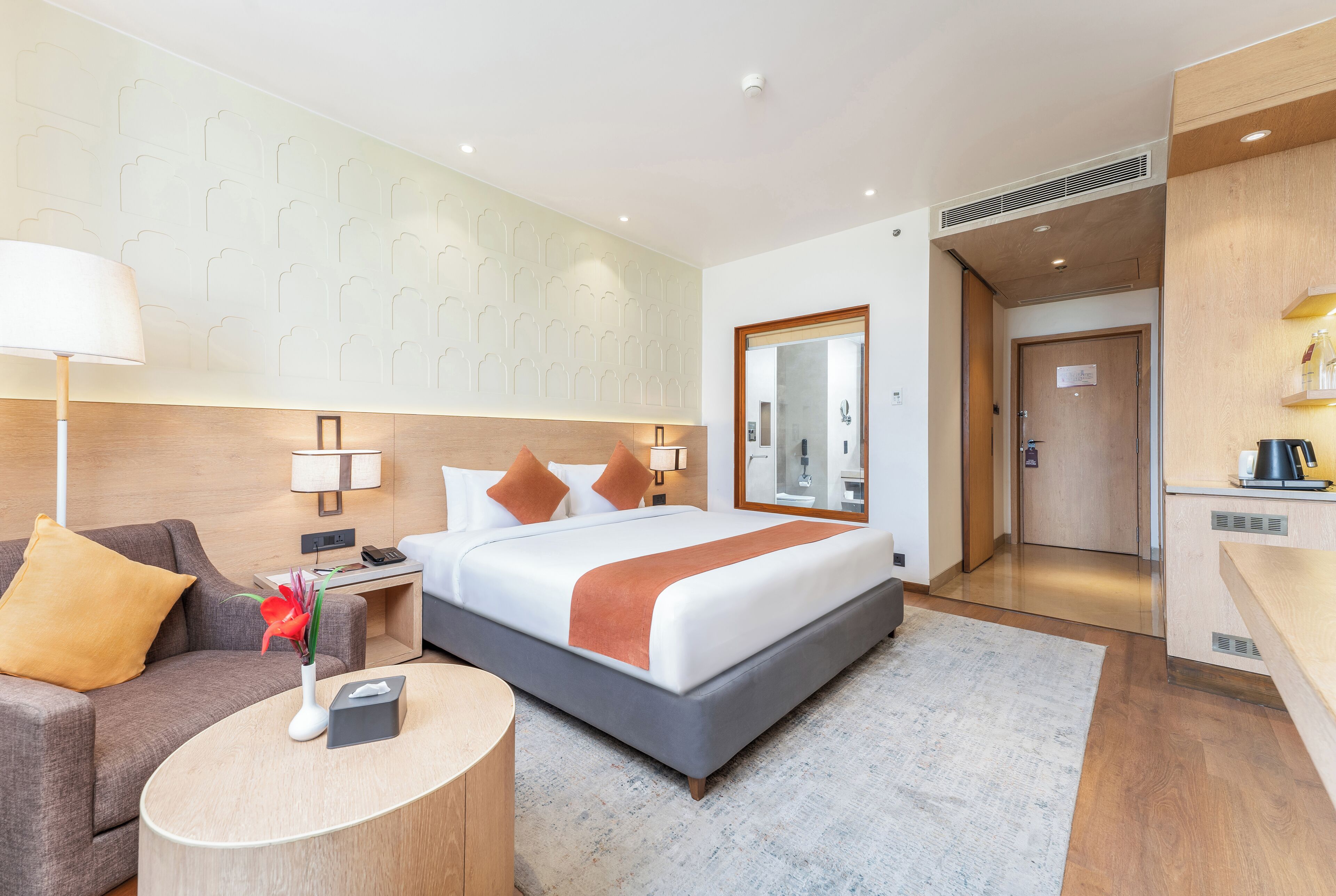 Une chambre d’hôtel avec un lit, un bureau, une chaise, une lampe et un miroir.