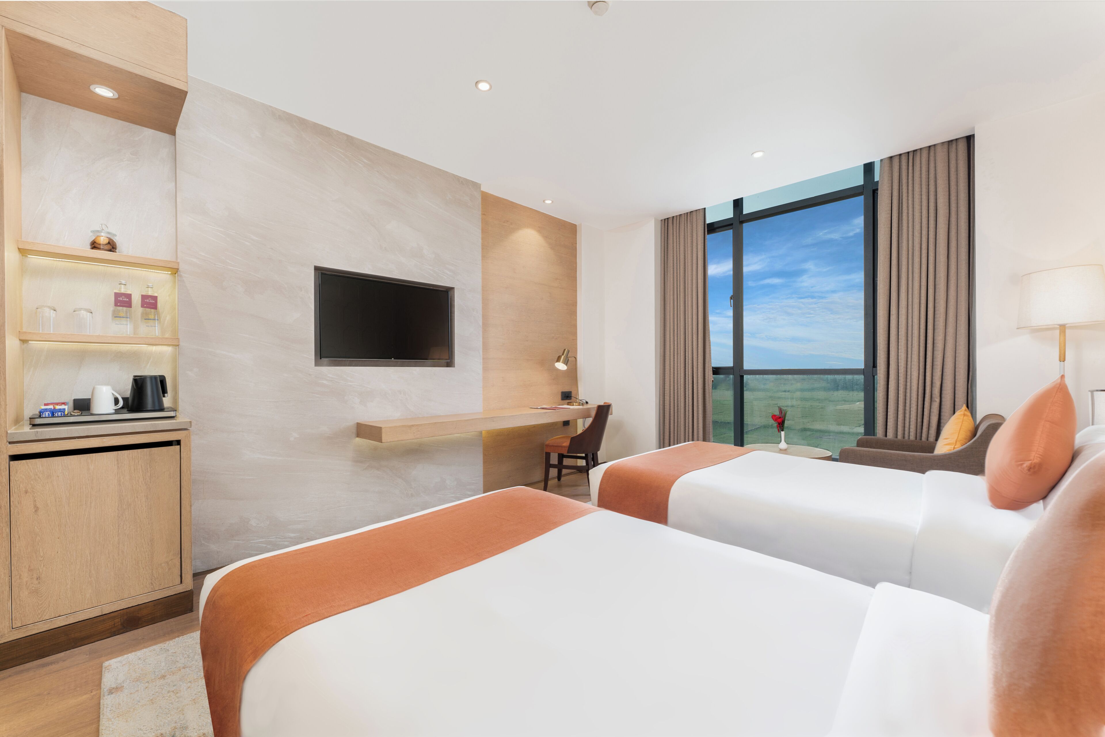 A hotel room with two beds, a desk with a chair, a TV, and a large window with a view.