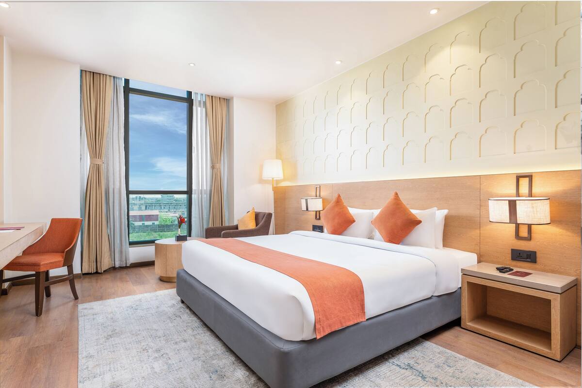 Een hotelkamer met een groot bed, een bureau, een stoel en uitzicht op de stad.