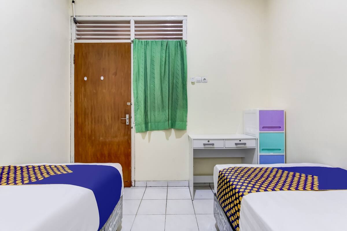 A room with two beds, a wooden door, a desk, and a green curtain.