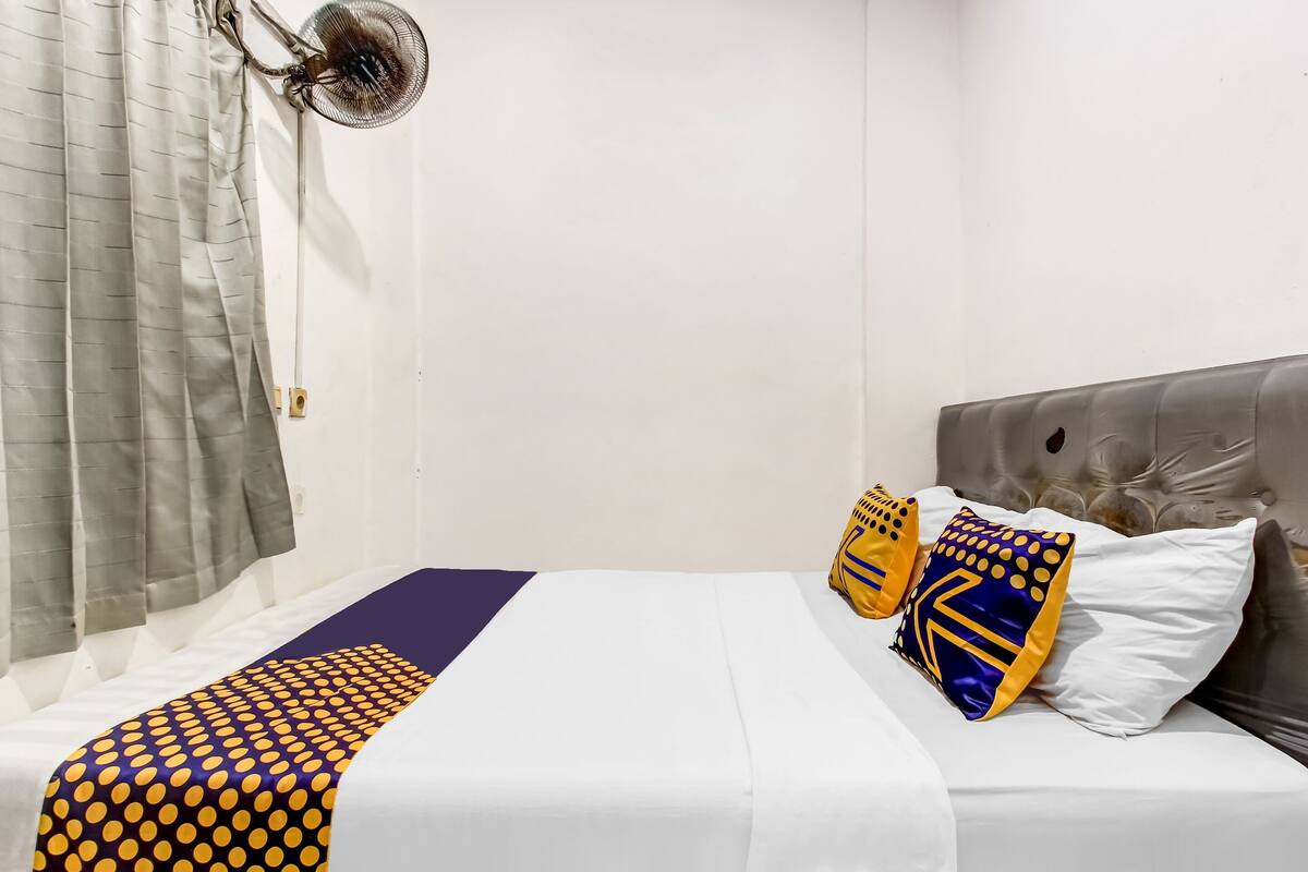 A neatly made bed with a patterned bedspread, a fan, and pillows with geometric designs.