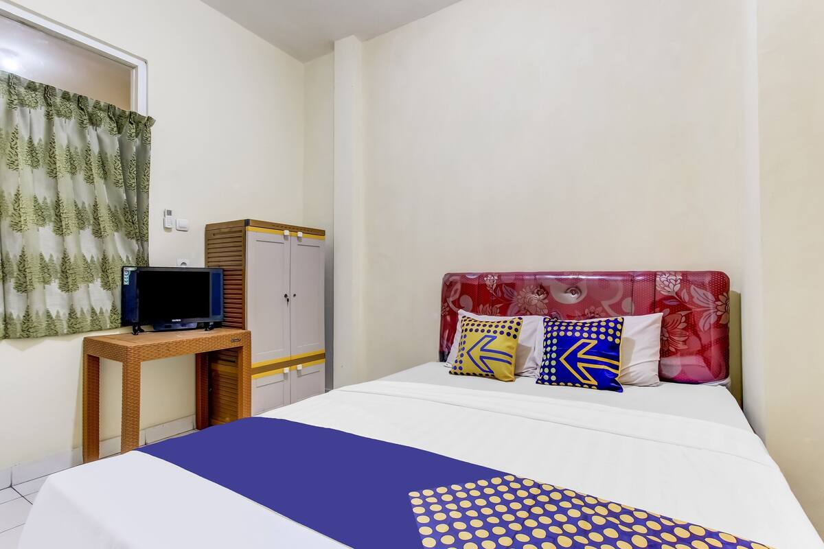 A bedroom with a bed, a television on a wooden table, and a wardrobe.