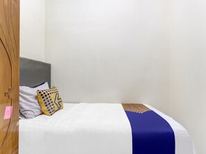 A single bed with a white and blue bedspread, a wooden door, and a plain white wall.