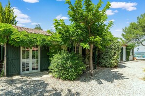 Un bâtiment avec un toit en tuiles, des volets verts et une allée gravillonnée.
