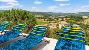 Una terraza con sillones de descanso y una vista panorámica de un pueblo y colinas.