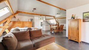 A spacious loft-style living area with a brown leather sofa, wooden dining table, and a kitchen in the background. - Cottage on sheep farm with gelateria (Merksplas)