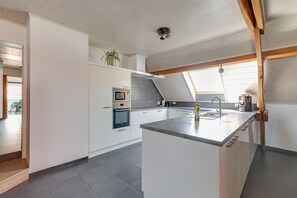 A modern kitchen with white cabinetry, a central island, and a skylight. - Cottage on sheep farm with gelateria (Merksplas)