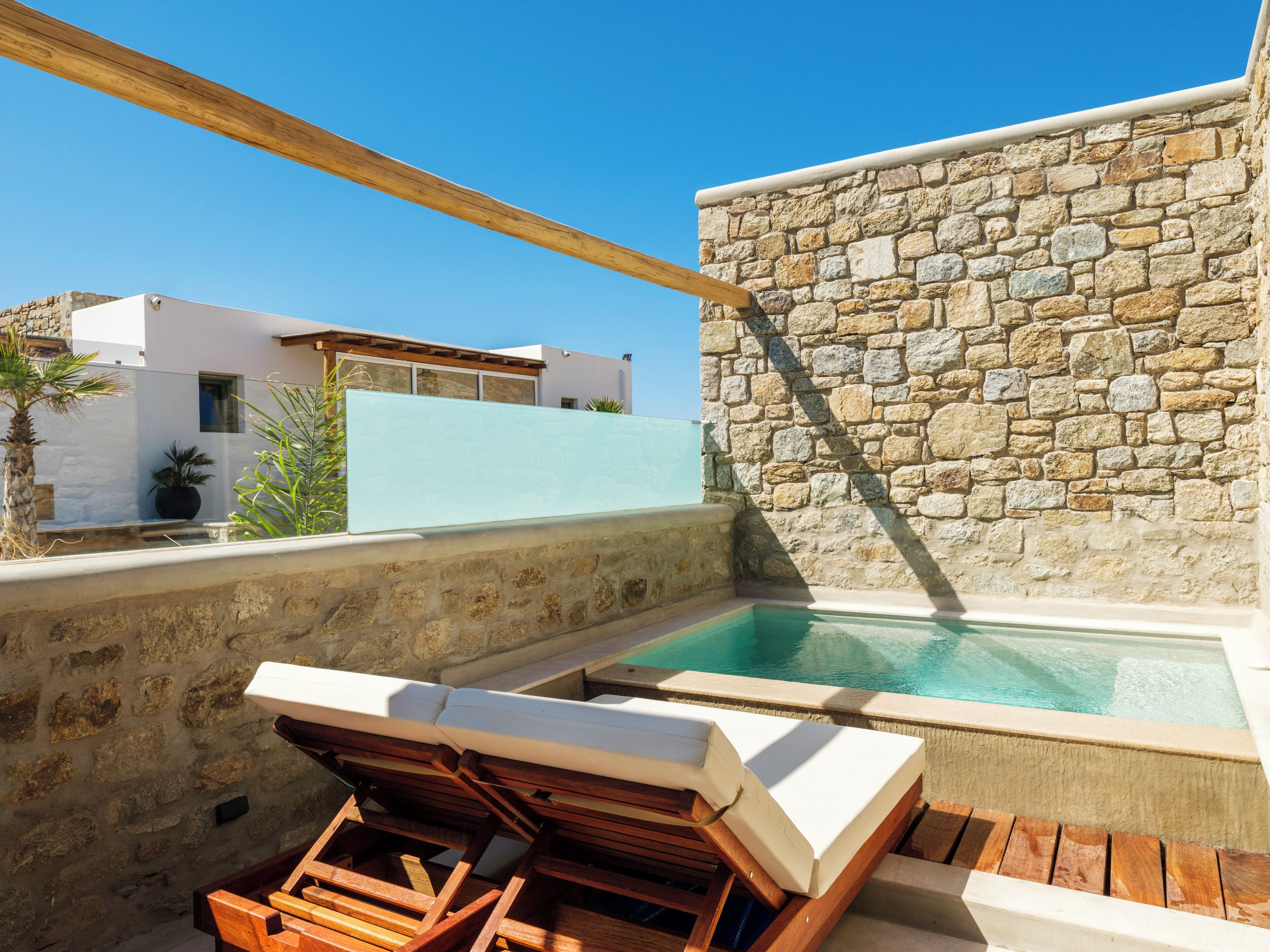 A stone wall, a pool, and wooden lounge chairs.
