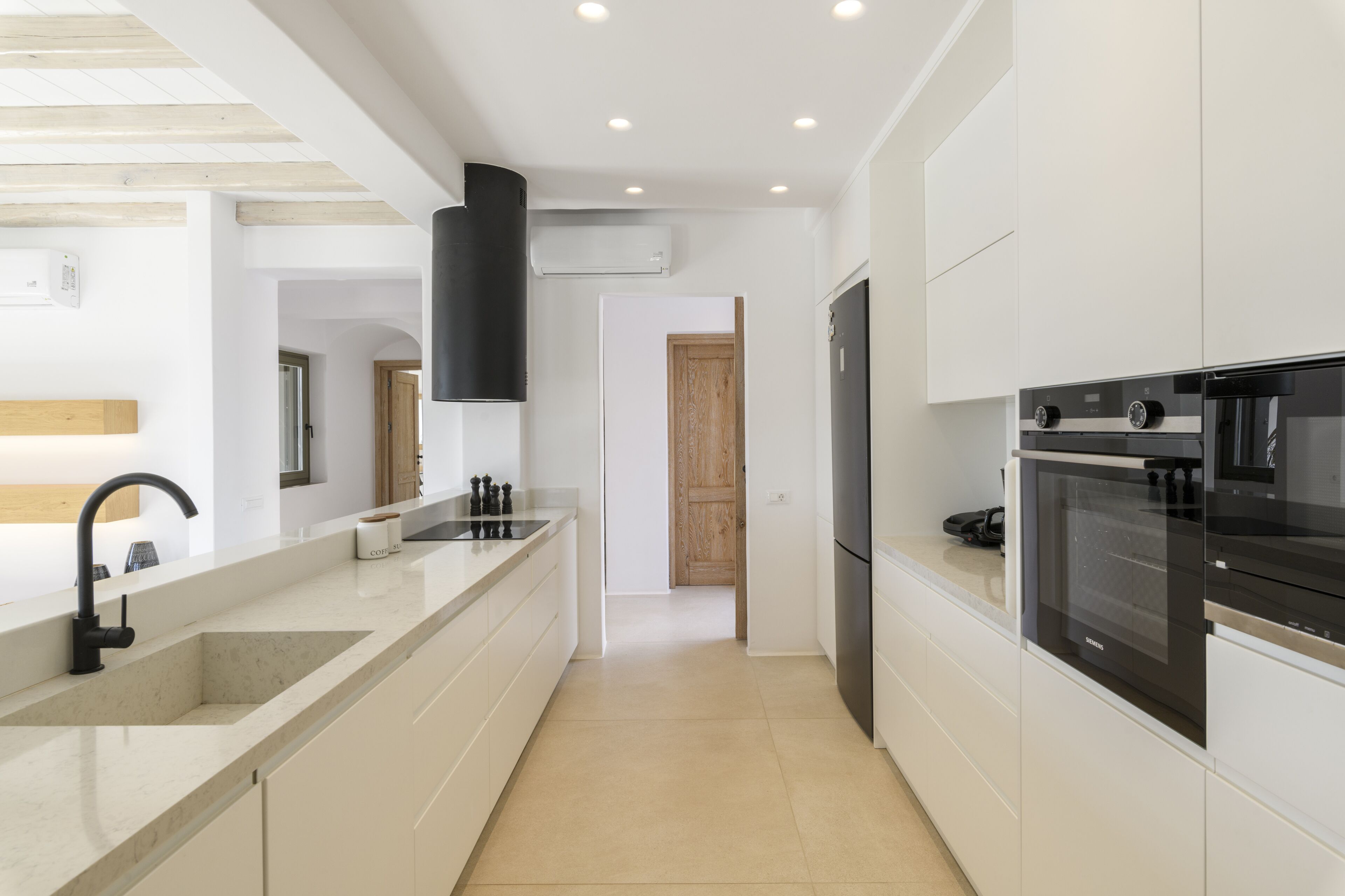 Una cocina moderna con armarios blancos, un horno negro y un lavamanos de acero inoxidable.