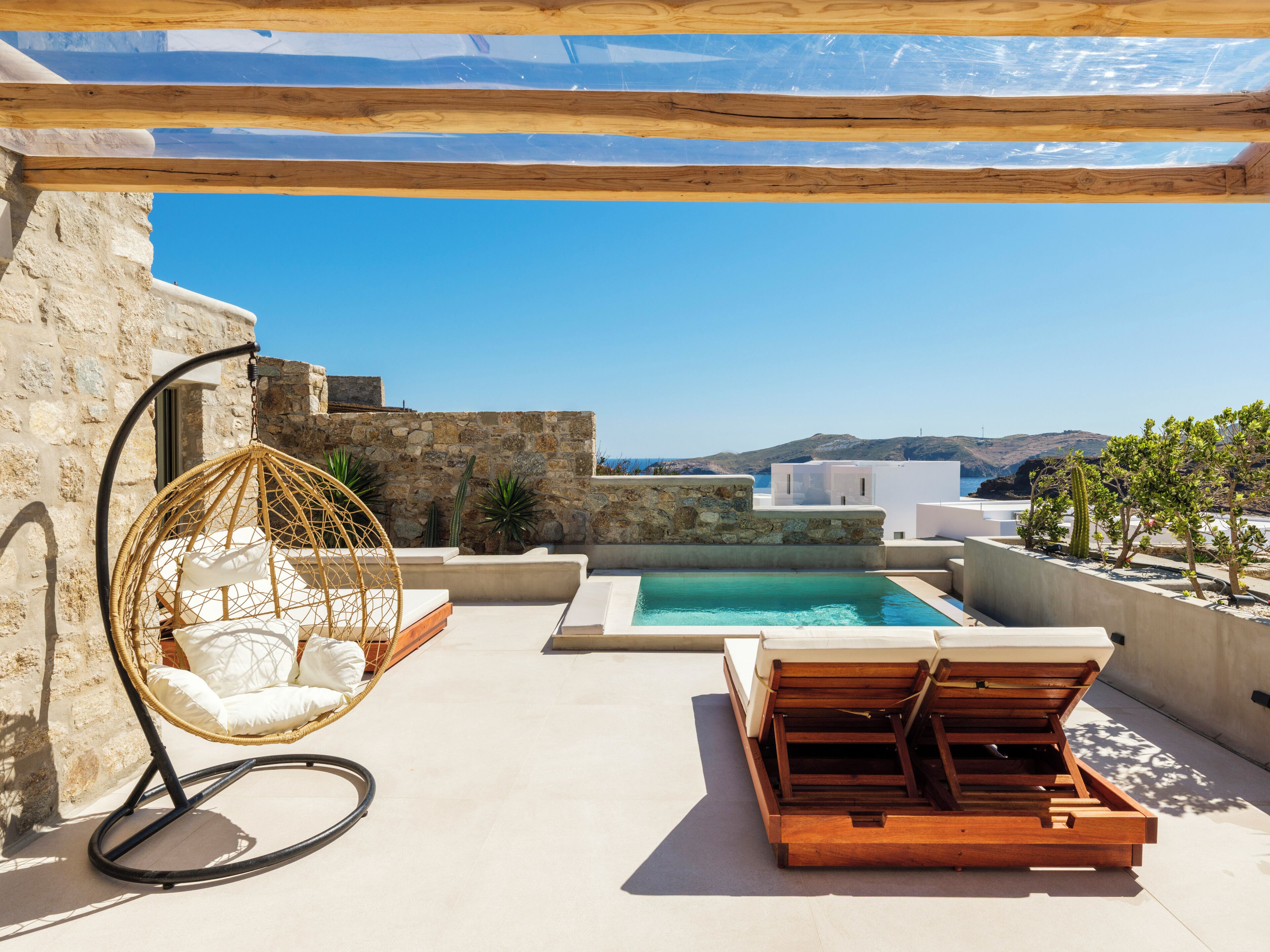 A rooftop pool area with a hanging chair, a wooden lounge chair, and a view of the sea.