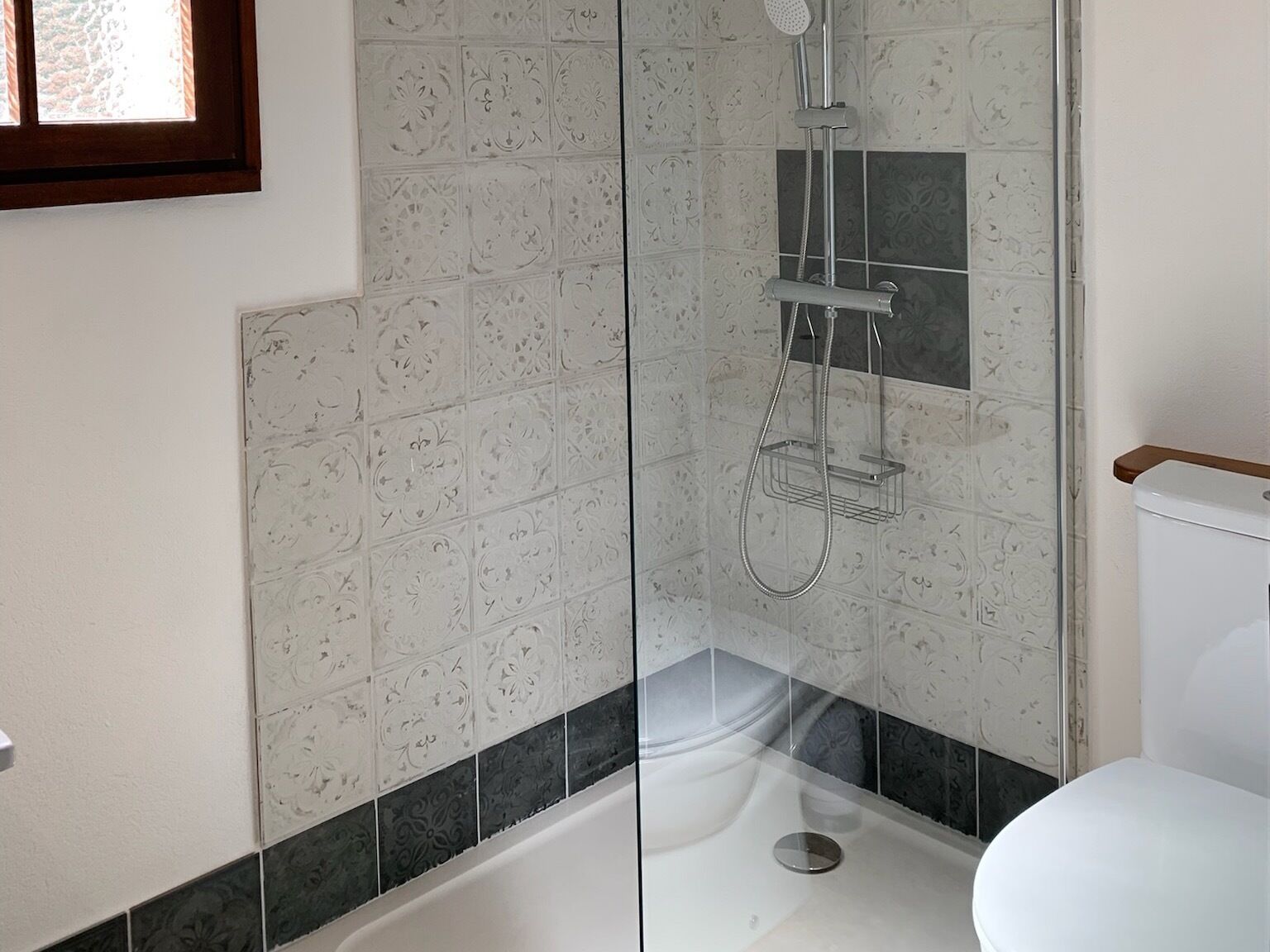 A bathroom with a glass-enclosed shower, a white toilet, and patterned tiles.