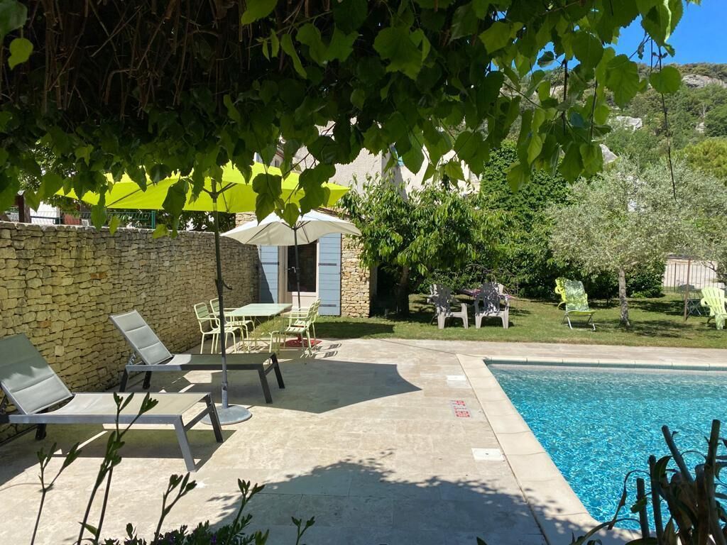 A pool area with lounge chairs and a table, surrounded by a stone wall and greenery.