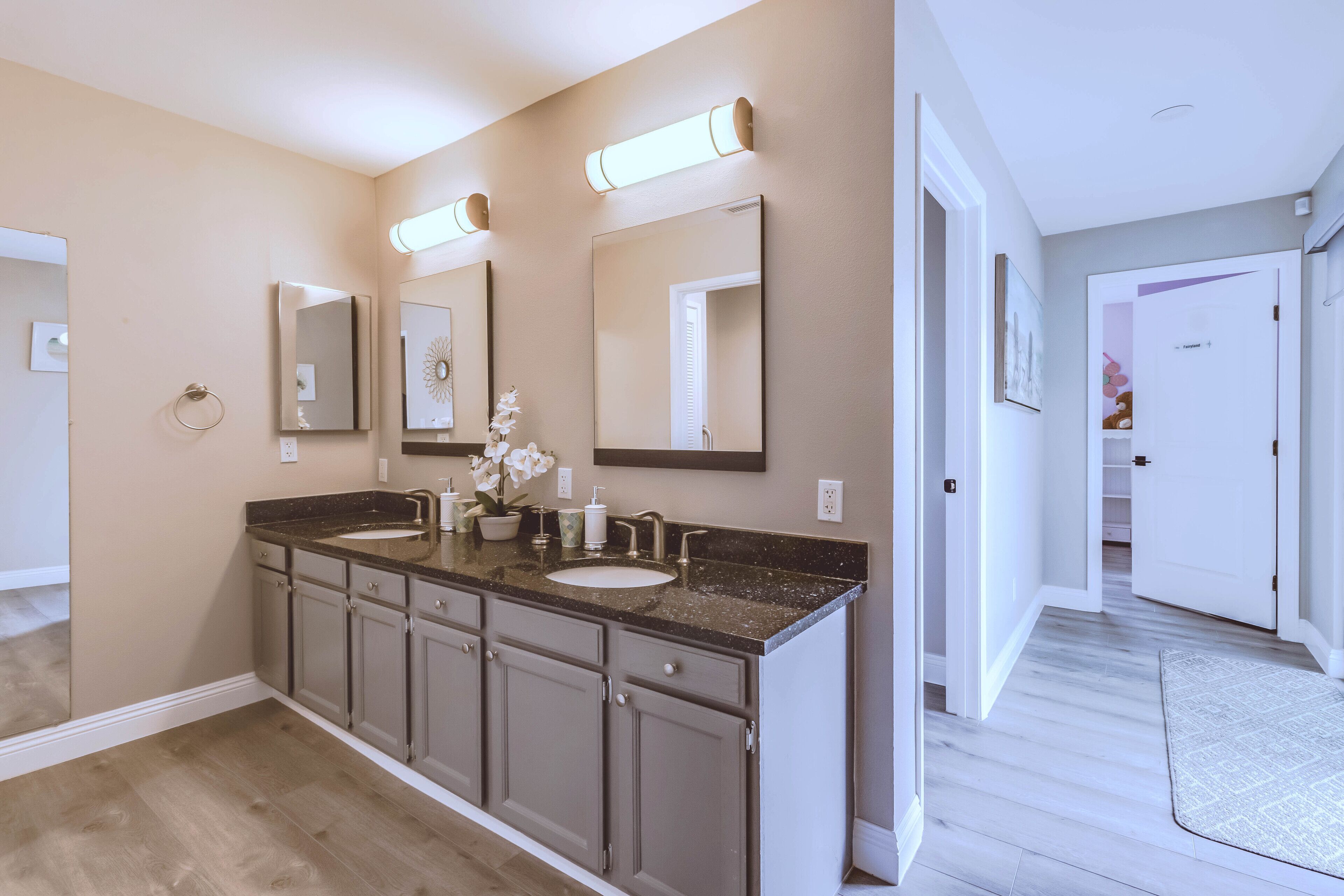 A modern bathroom with a double sink vanity, large mirrors, and a potted orchid.