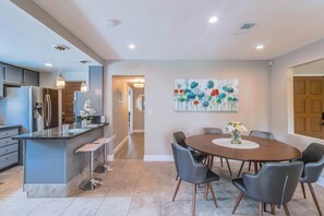 A modern kitchen with a central island, bar stools, and a dining area with a round table and chairs.