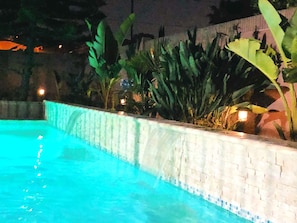 A swimming pool with a tiled edge, surrounded by lush greenery and a stone wall.