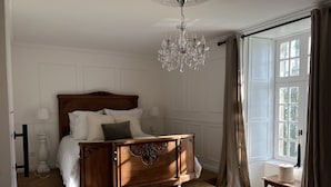A bedroom with a wooden bed, a chandelier, a window with curtains, and a wooden dresser.