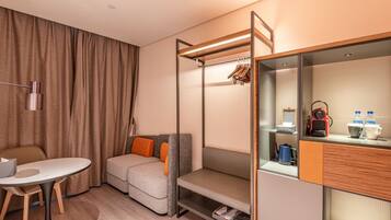 Ein kleines Hotelzimmer mit Schlafsofa, Esstischchen, Stockbett und Kleiderschrank, Spiegel sowie einer Kaffeemaschine.