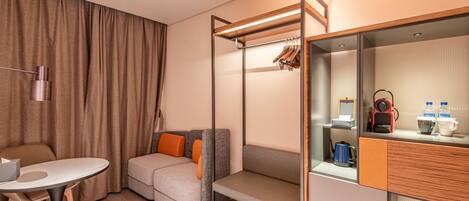 Habitación de hotel compacta con sofá, una mesita, una cama litera con armario, espejo y cafetera.