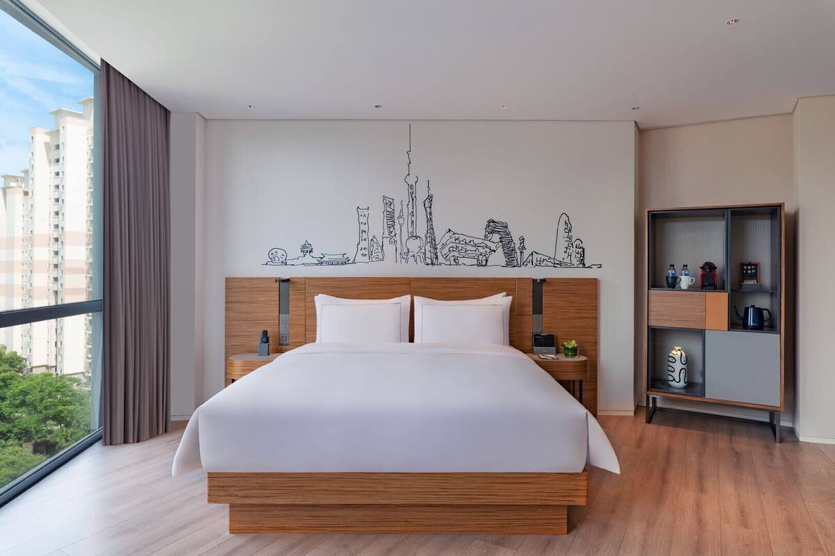 A modern hotel room with a large bed, wooden headboard, and a cityscape mural on the wall.