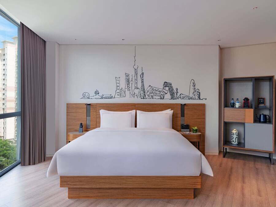 Una habitación de hotel moderna con una cama grande, cabecera de madera y un mural con vistas a la ciudad.