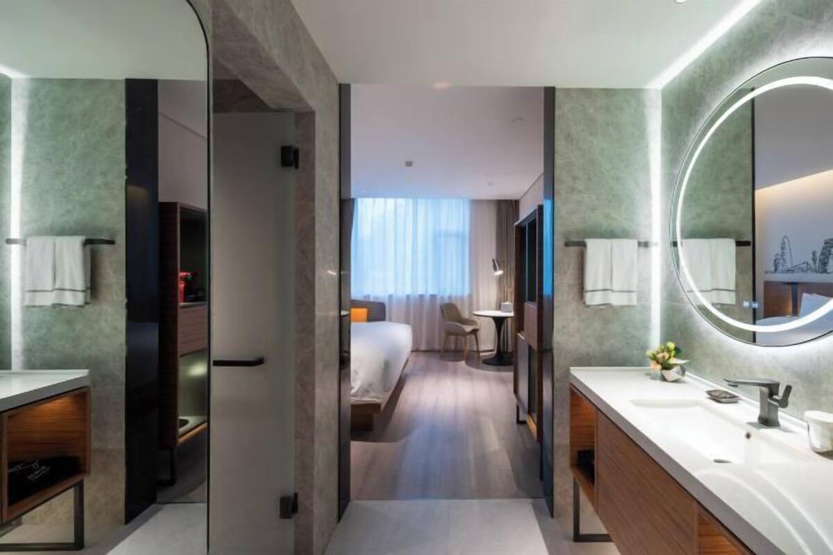A modern hotel bathroom with a large mirror, a sink, and a shower area.