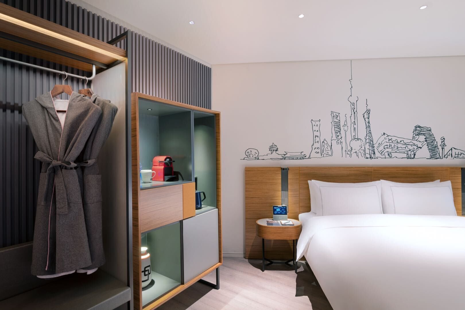 Een moderne hotelkamer met een bed, een badjas, een nachtkastje met een lamp en een stadsgezicht muurschildering.