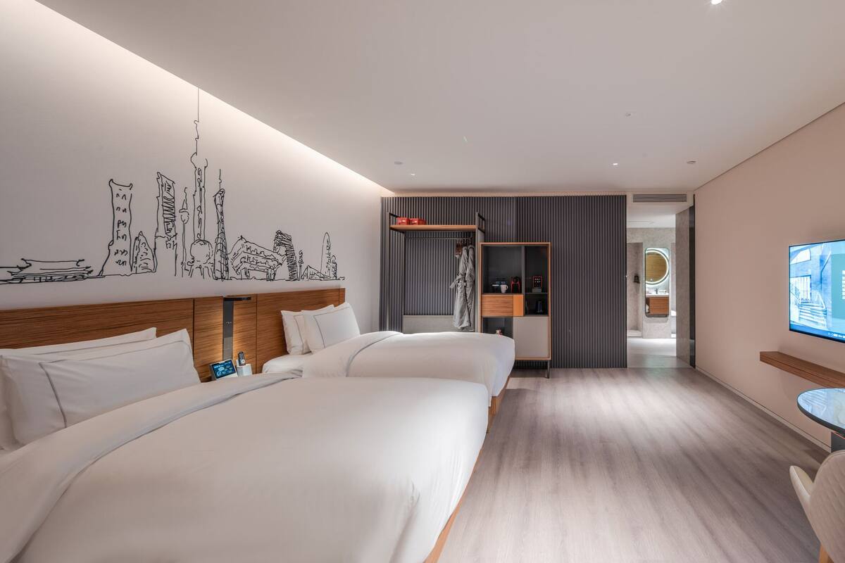 A modern hotel room with two beds, a TV, and a small table.