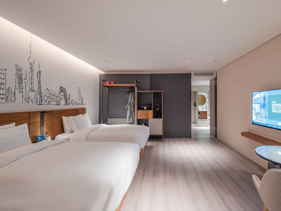 A modern hotel room with two beds, a TV, and a small table.