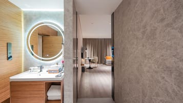Een moderne badkamer met een ronde spiegel, een houten wastafelmeubel en een klein tafeltje met stoelen.