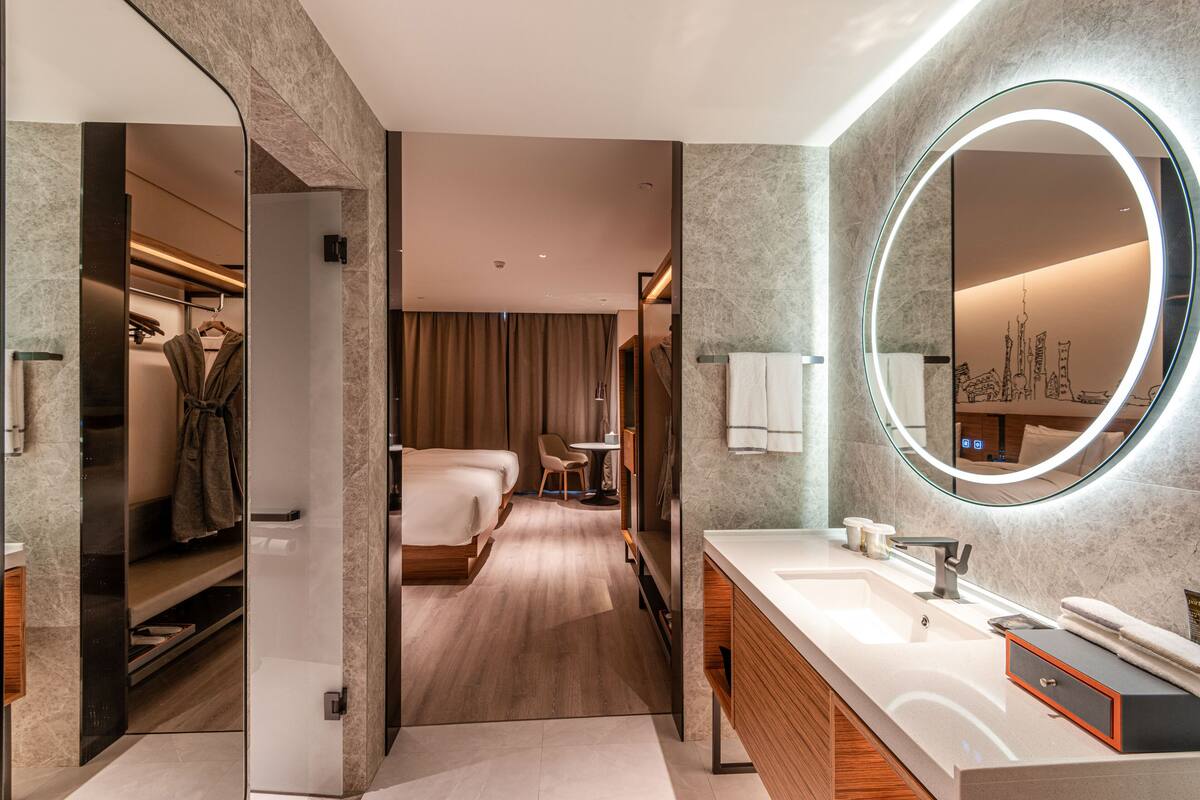 A modern hotel bathroom with a large mirror, a sink, and a shower area.
