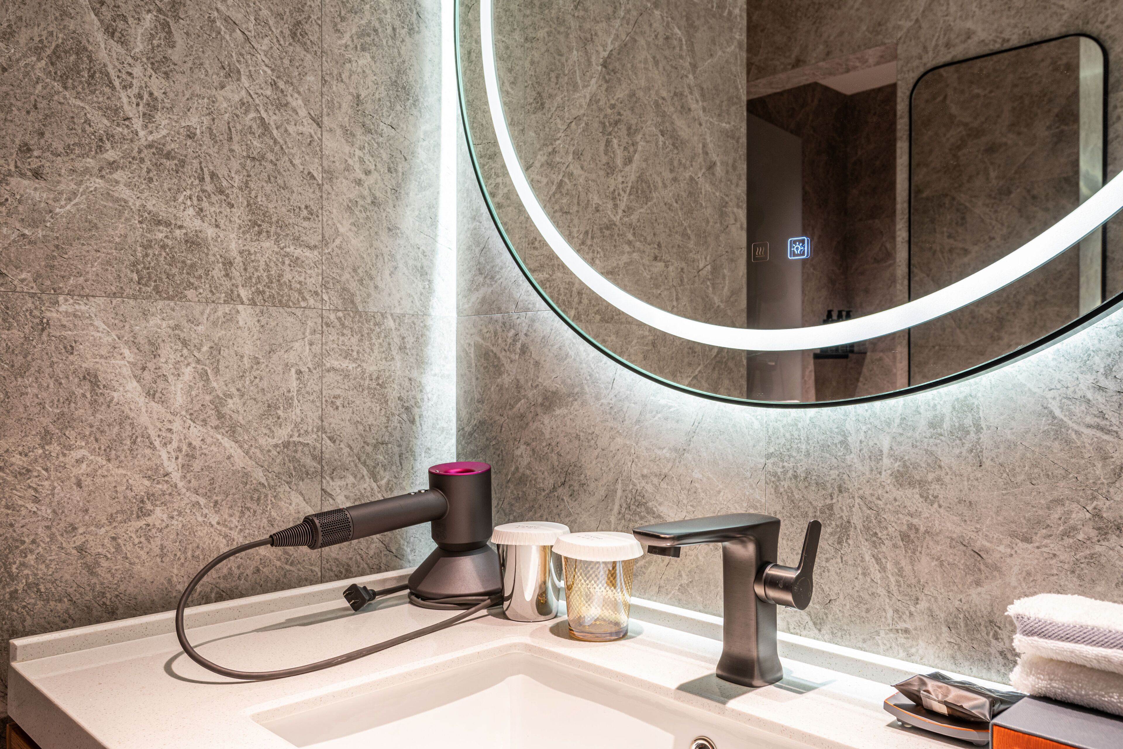 A bathroom with a marble wall, a round mirror, a hairdryer, and a towel rack.