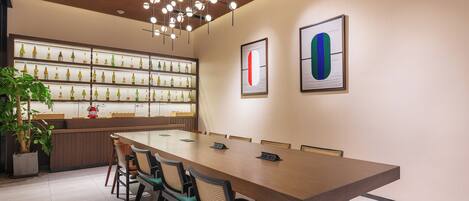 Uma sala de conferências moderna com uma mesa comprida, cadeiras e uma parede de garrafas de vinho.