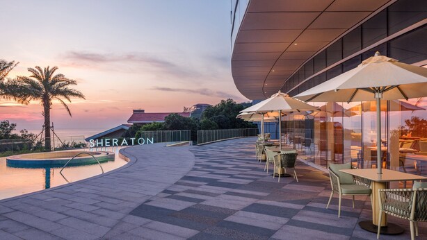An outdoor seating area with umbrellas and chairs, a pool, and a building with the name "SHERATON" visible. - Sheraton Beihai Resort (Beihai)