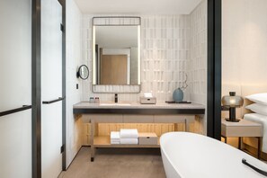 Un baño moderno con un espejo grande, un lavamanos, un perchero para toallas y una mesita de noche con lámpara.