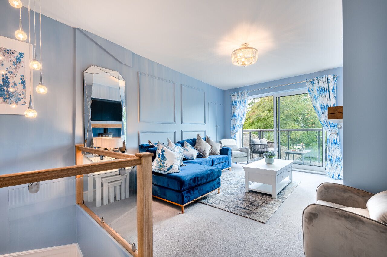 Un salon moderne avec un canapé bleu, une table basse blanche et une grande fenêtre avec des rideaux.