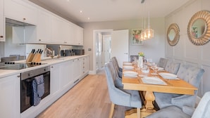 Eine moderne Küche mit weißen Schränken, einem Holzespeise Tisch für sechs Personen und einem großen Spiegel an der Wand.