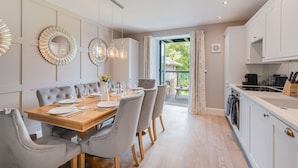 Ein stilvolles Esszimmer mit einem Holztisch, gedeckten Plätzen für sechs Personen, grauen Sitzmöbeln und Pendelleuchten.