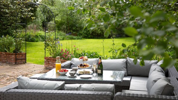 An outdoor seating area with a table set for breakfast, surrounded by lush greenery and a brick planter. - Redmayne House in Kirkby Stephen (Kirkby Stephen)