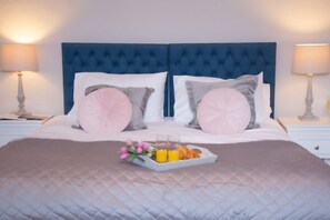 A neatly made bed with a blue headboard, two pillows, a tray with croissants and orange juice, and a bedside table with a lamp. - Redmayne House in Kirkby Stephen (Kirkby Stephen)