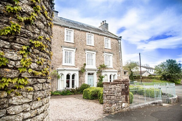 A stone building with white shutters, a gravel driveway, and a metal fence. - Redmayne House in Kirkby Stephen (Kirkby Stephen)
