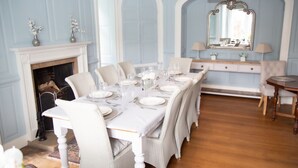 A dining room with a long table set for six, white chairs, a fireplace, a mirror, and a dresser with lamps. - Redmayne House in Kirkby Stephen (Kirkby Stephen)