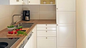 A compact kitchen with white cabinets, a coffee maker, and a wooden countertop with fresh vegetables.