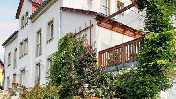 A two-story building with a red-tiled roof, white walls, and a balcony with wooden railings.