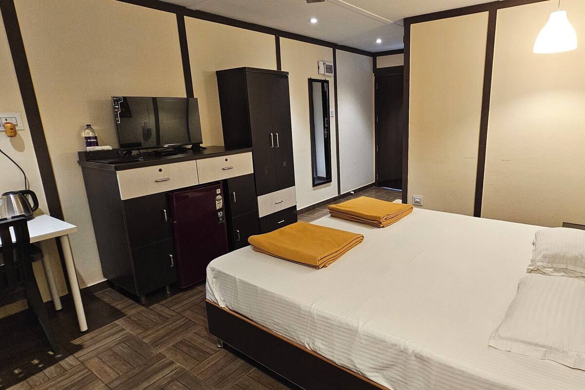 A hotel room with a bed, a desk with a television, a wardrobe, and a small kitchenette.