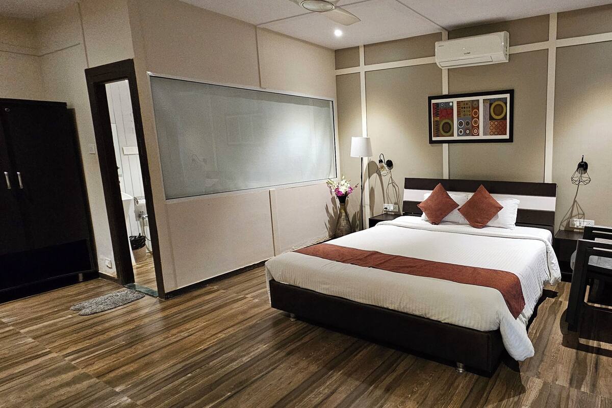 A hotel room with a large bed, a desk, a chair, a TV, and a painting on the wall.