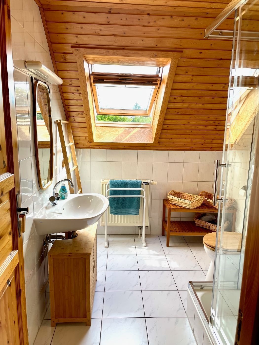 A bathroom with a skylight, a sink, a towel rack, a shower, and a wooden cabinet.