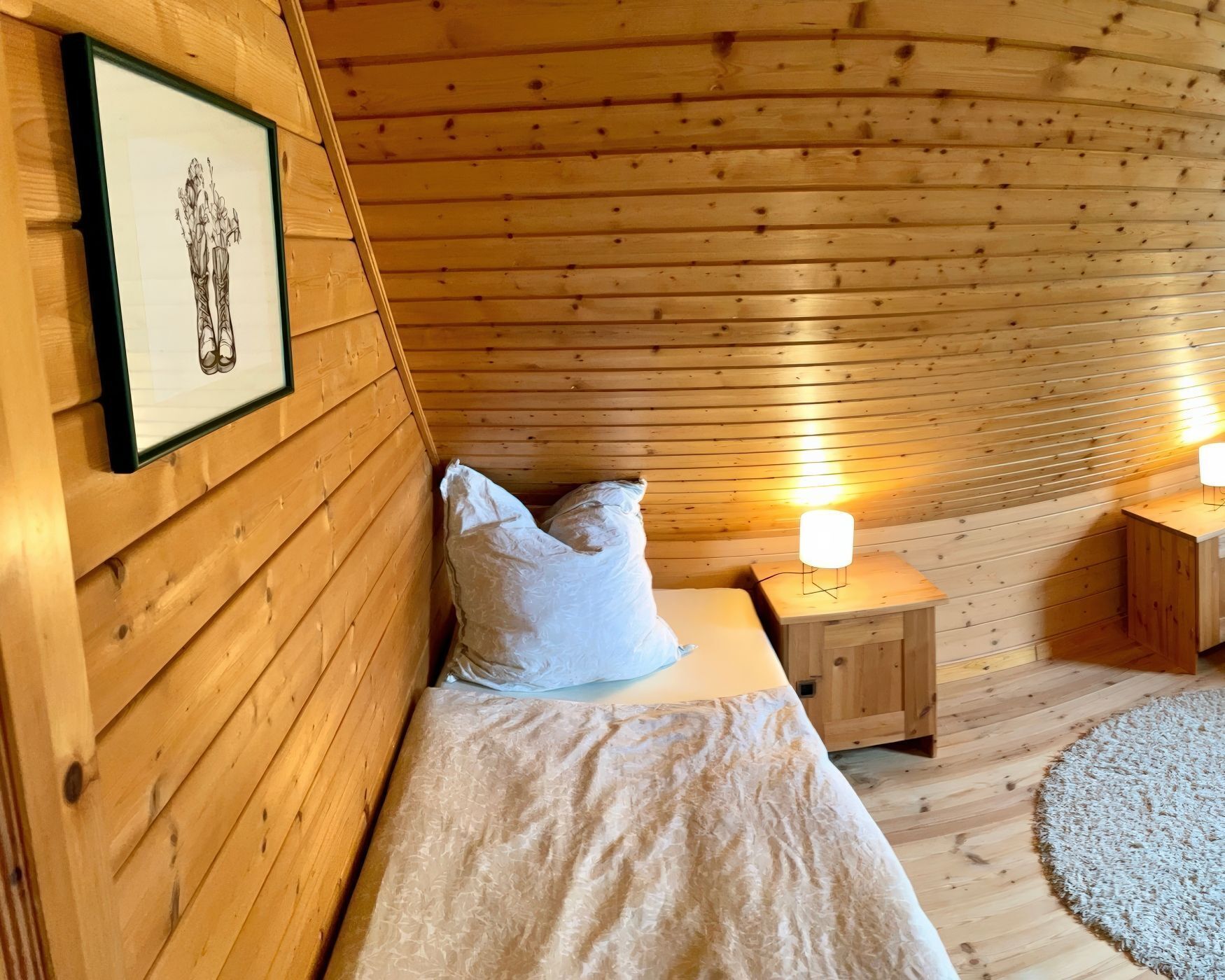 Een gezellig houten kamer met een bed, kussens, een ingelijste foto en twee bedlampen.