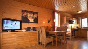 Interior em madeira com televisão, mesa de jantar, cadeiras e cozinha.
