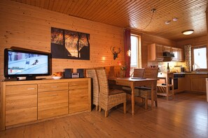 A wooden interior with a television, dining table, chairs, and kitchen area.